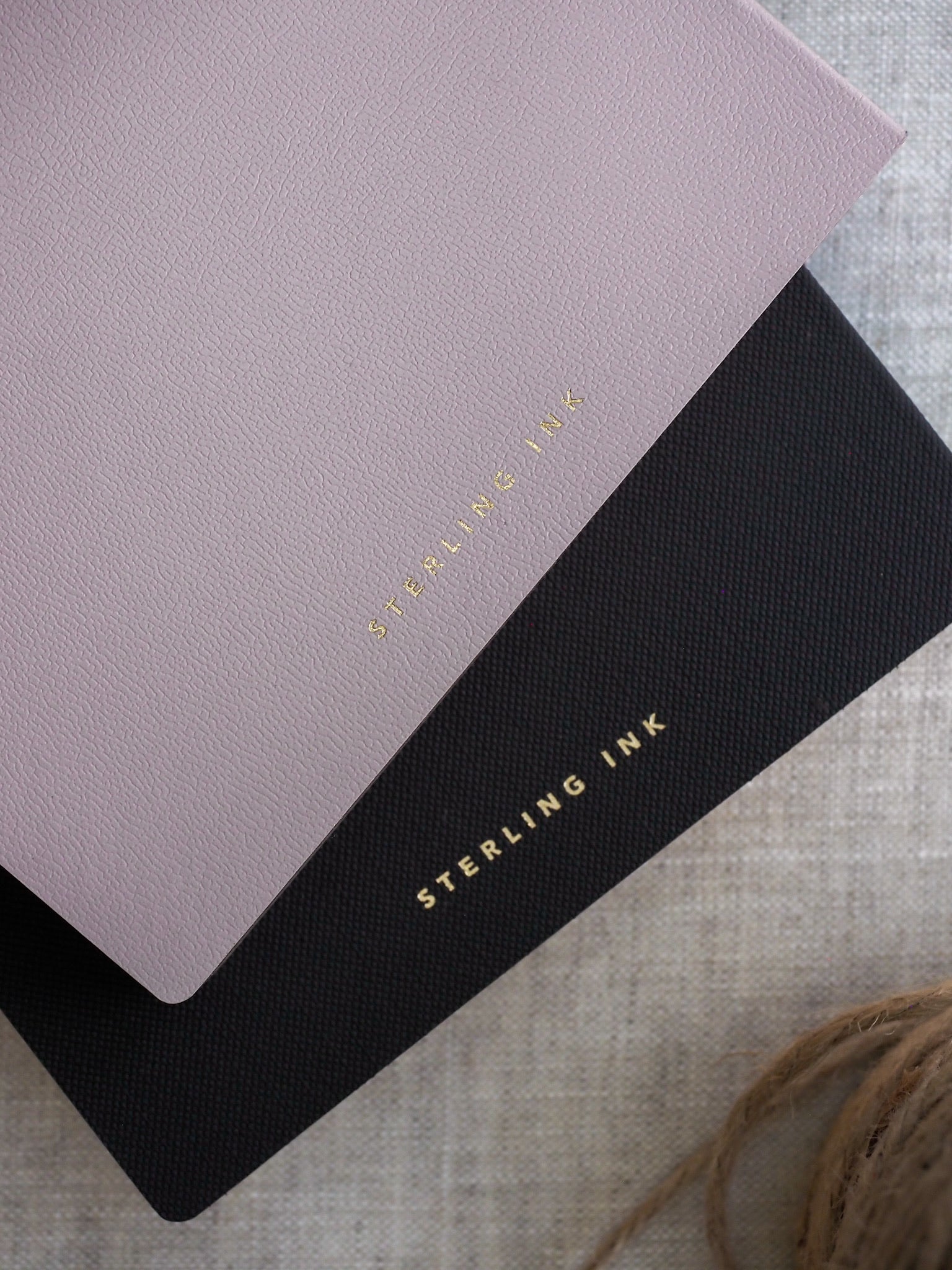 Stacked A5 grid notebooks featuring soft blush and sleek black covers, both decorated with elegant gold foiled "Sterling Ink" lettering.