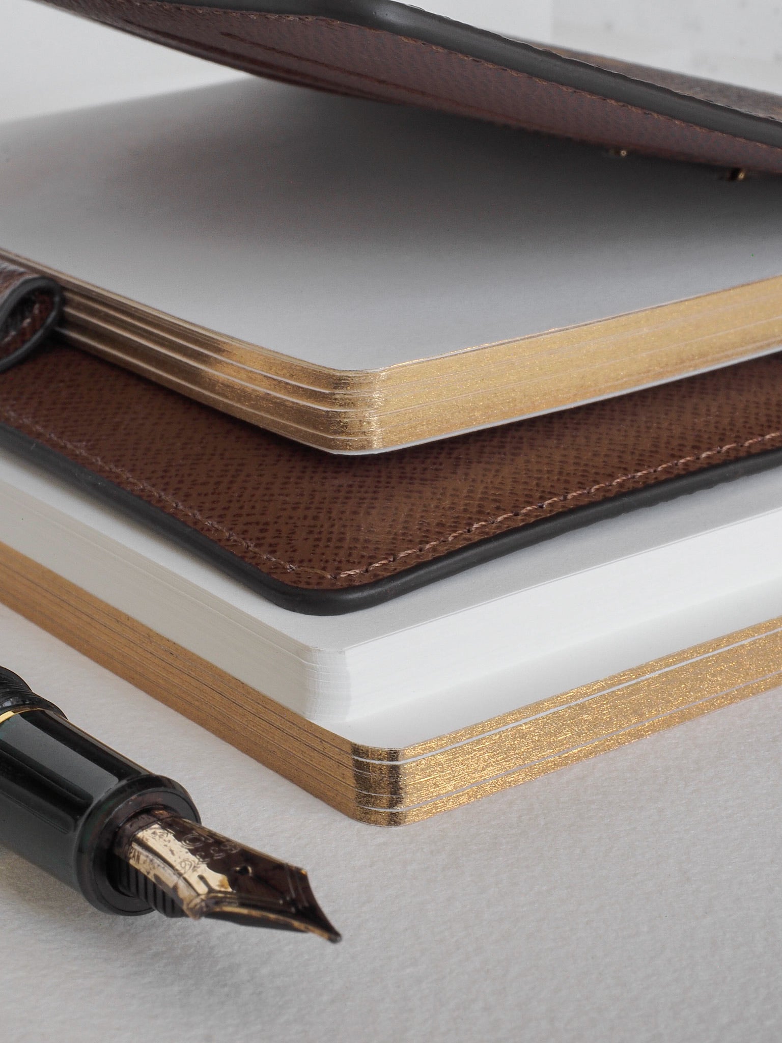 Stack of pristine, gold-edged lined loose leaf paper, presented with dark brown leather-look accents, ideal for journaling or record-keeping.