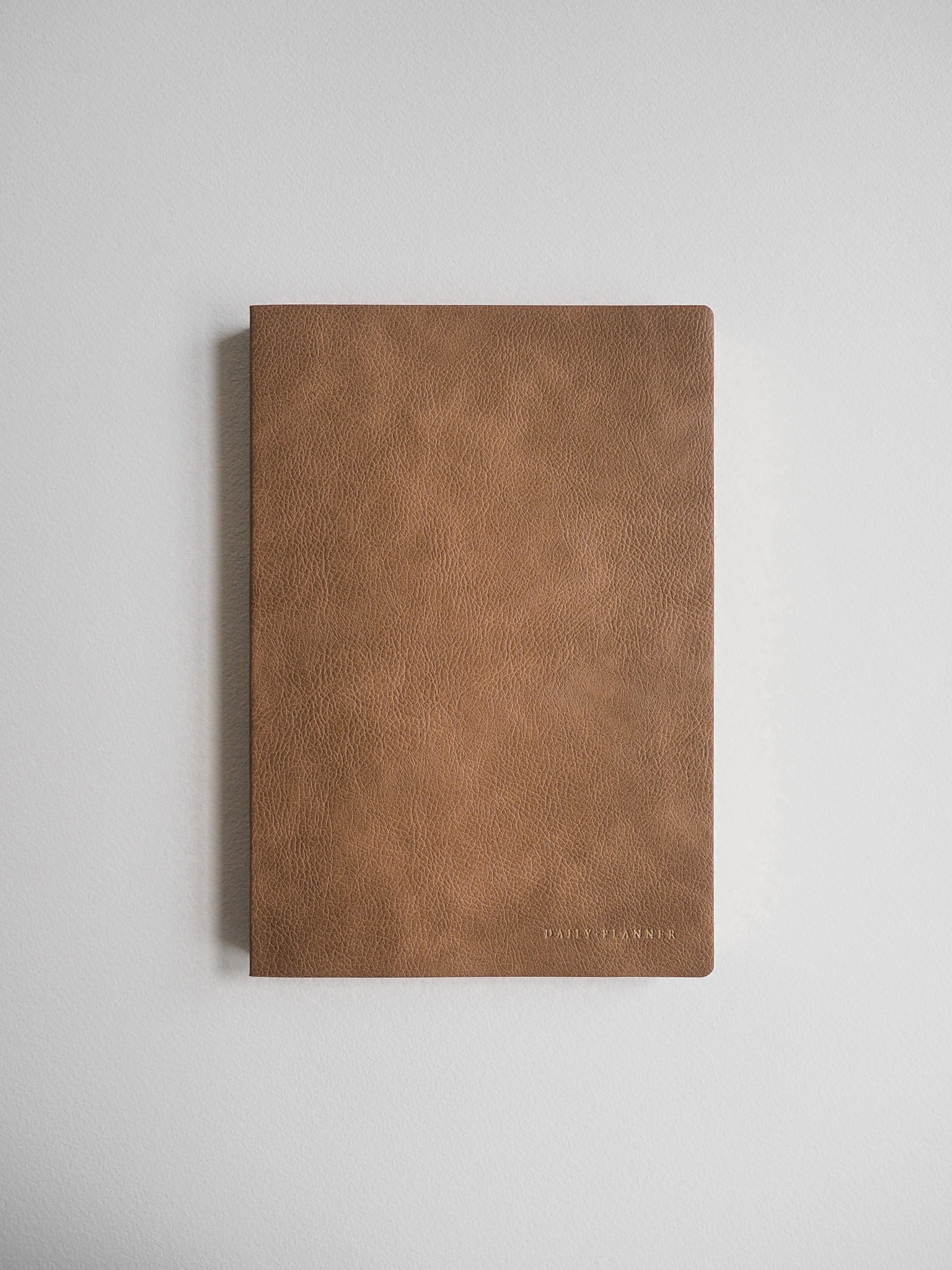 Minimalist A5 undated daily planner featuring a solid, matte camel brown faux leather cover and subtle branded detail.