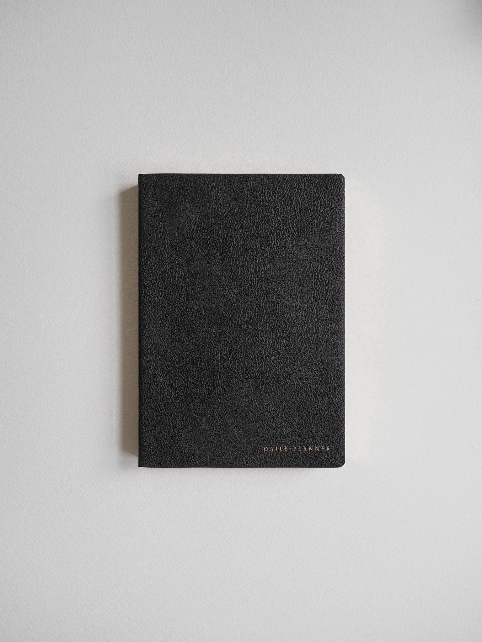 Minimalist matte black daily planner featuring a textured cover and a discreet embossed logo, perfect for writing and organization.