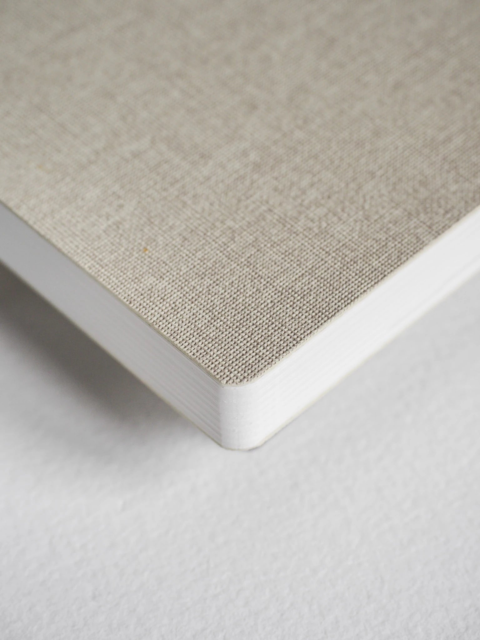 Close-up of a notebook corner showing a light beige linen-textured cover and white page edges on a white background.
#Color_Linen