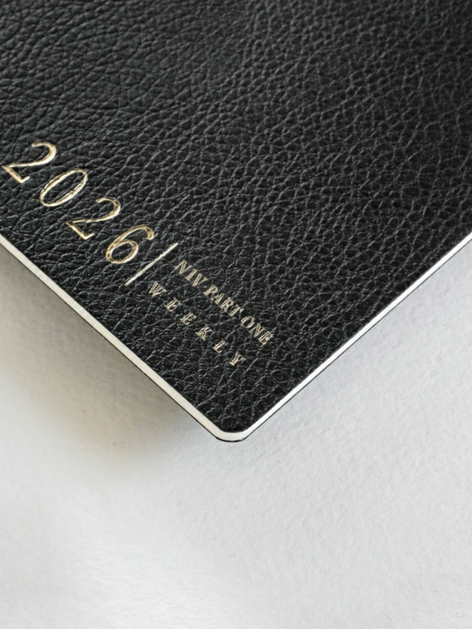 Luxurious black textured weekly booklet cover accented with shimmering gold foil lettering proclaiming "2026" and "N1 Vertical Weekly."