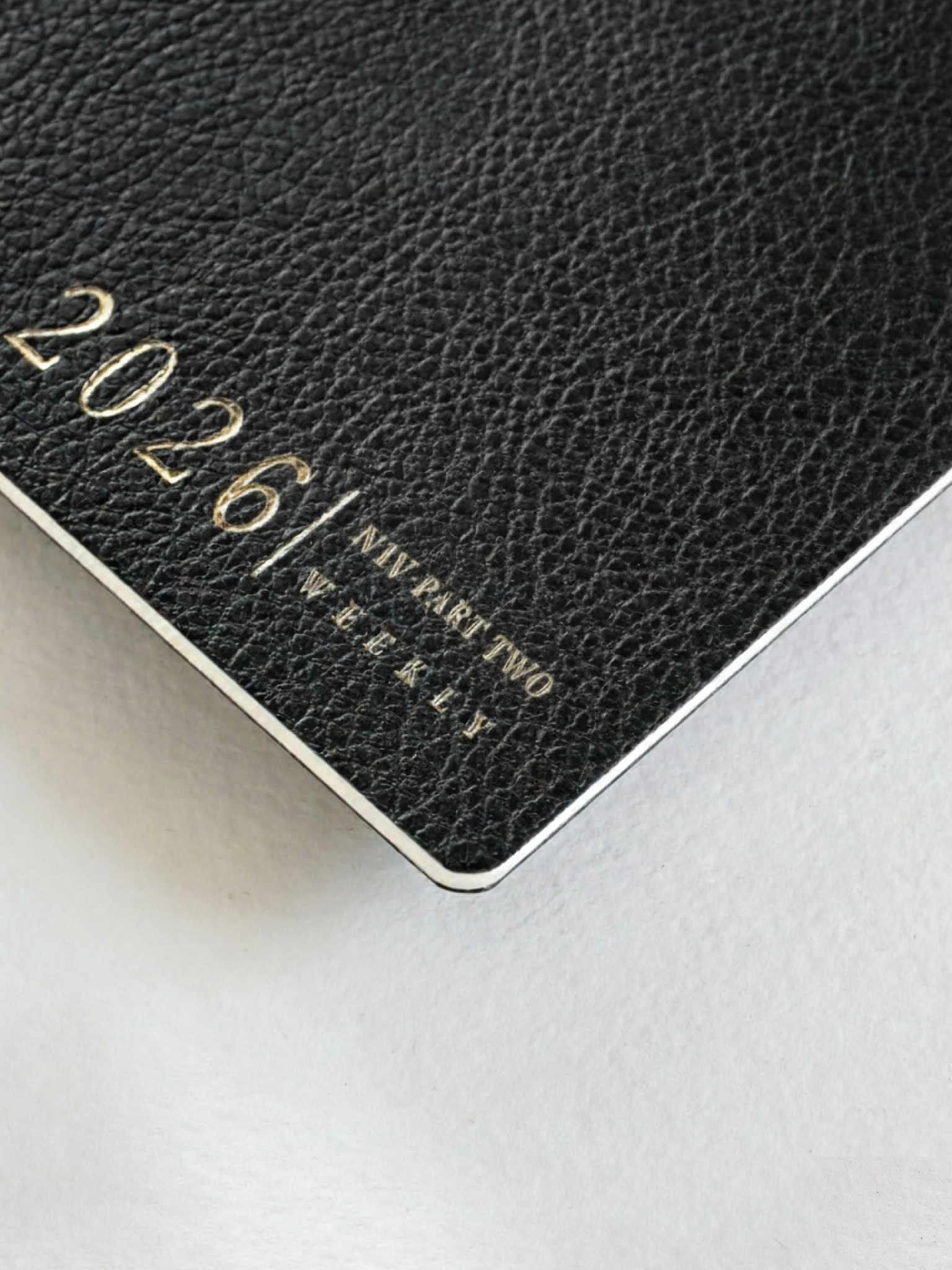 Black, textured weekly planner booklet cover featuring elegant gold foil embossing that spells out "2026/ NIV PART TWO WEEKLY," suggesting an organized 2026 journal set.