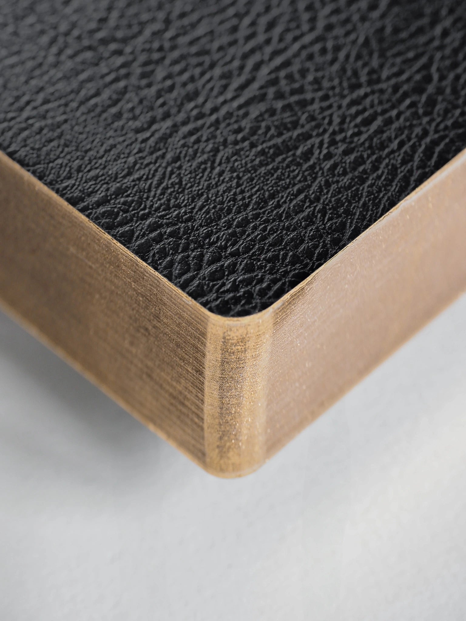 Close-up of a corner showing a black textured leather top surface and a light natural wood side edge on a white background.
#Color_Onyx
