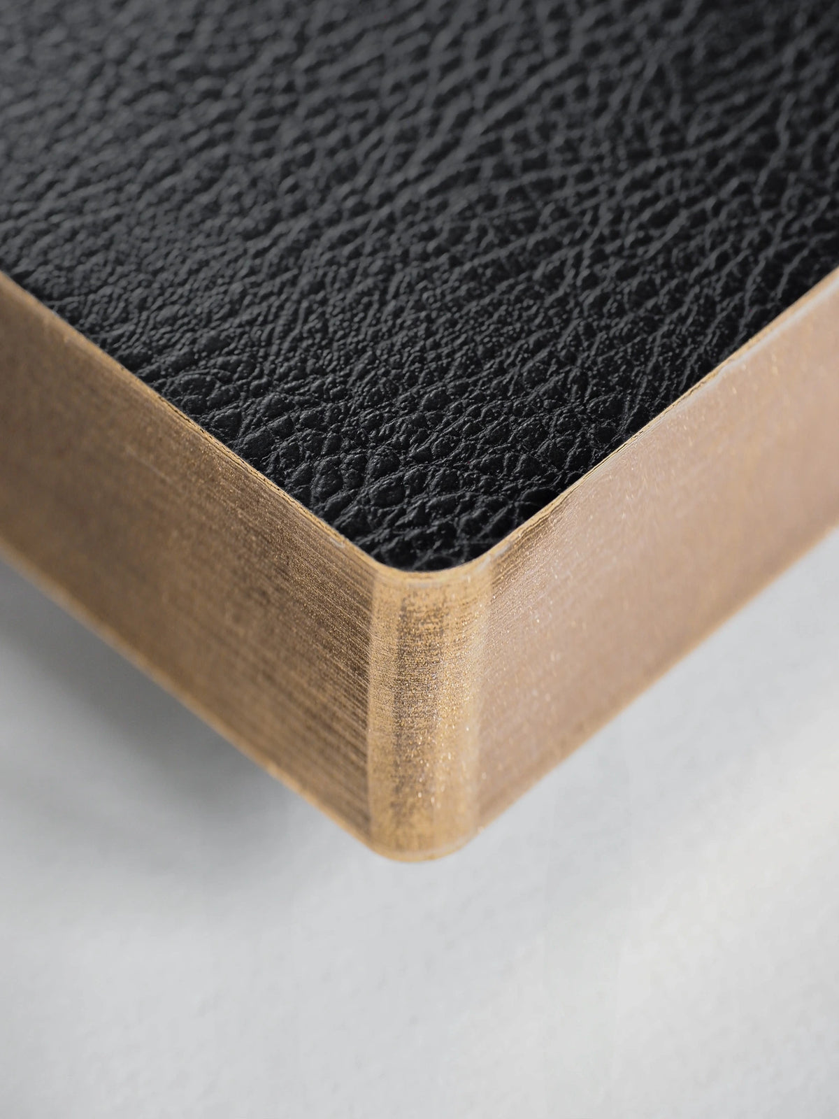 Close-up of a corner showing a black textured leather top surface and a light natural wood side edge on a white background.
#Color_Onyx
