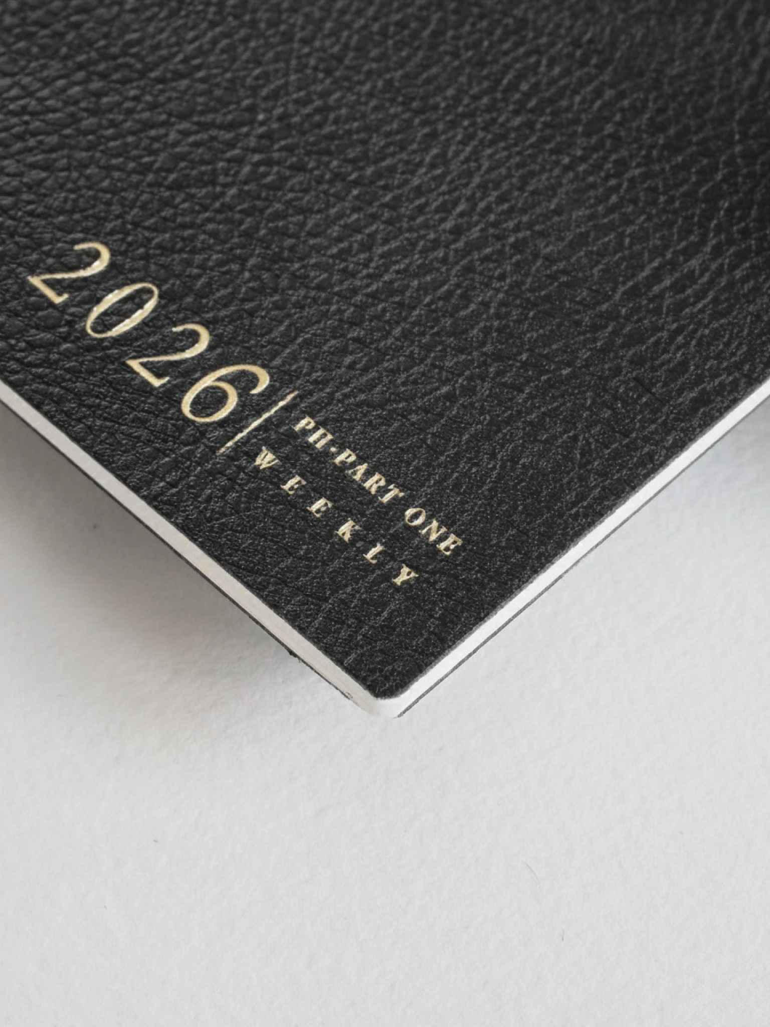 Dark black weekly planner booklet featuring the metallic lettering "2026 | PH-PART ONE WEEKLY" printed on the textured cover.