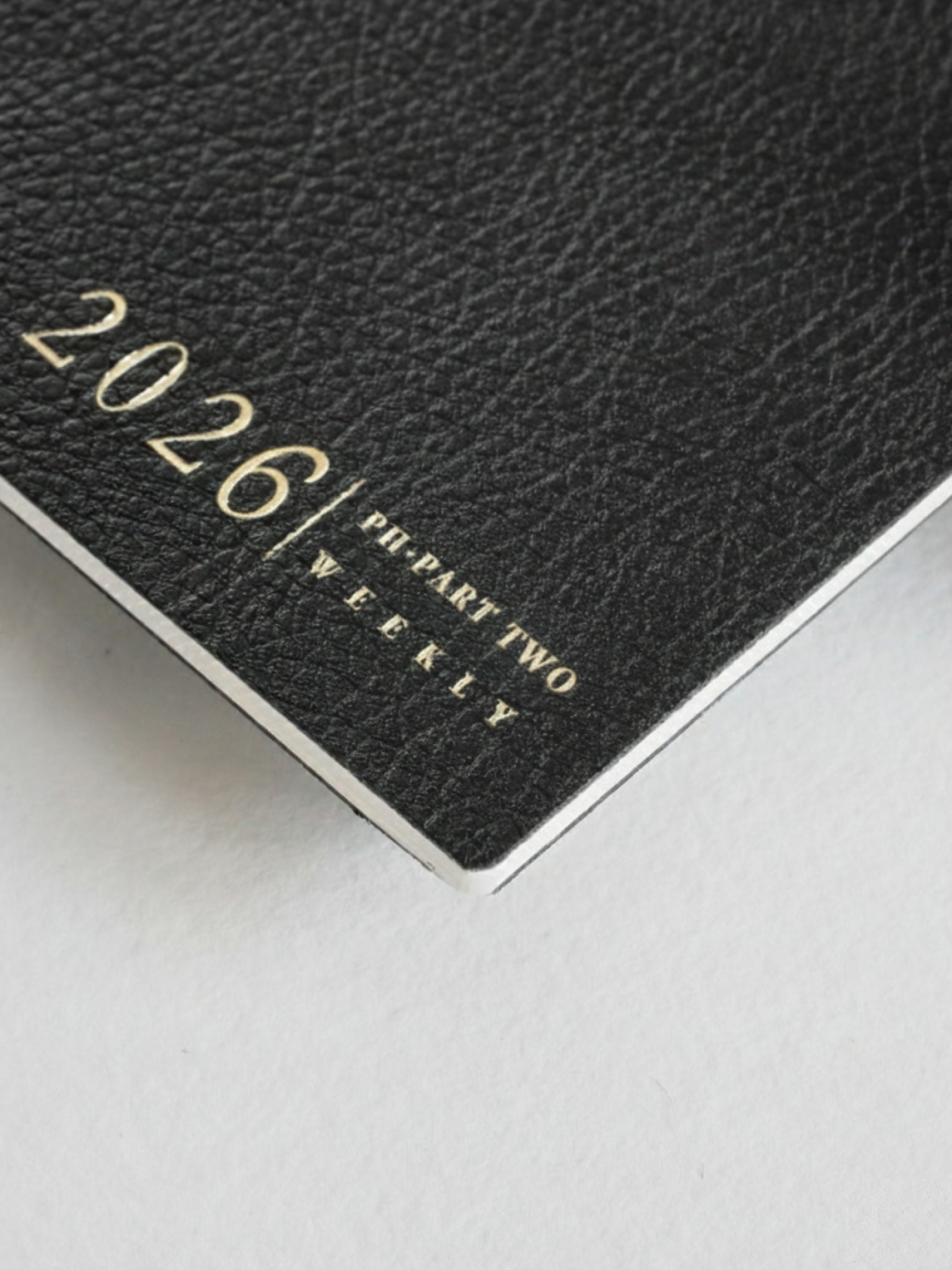 Black weekly planner booklet featuring a sophisticated, textured cover and prominent white text displaying "2026 | PI-PART TWO | WEEKLY."