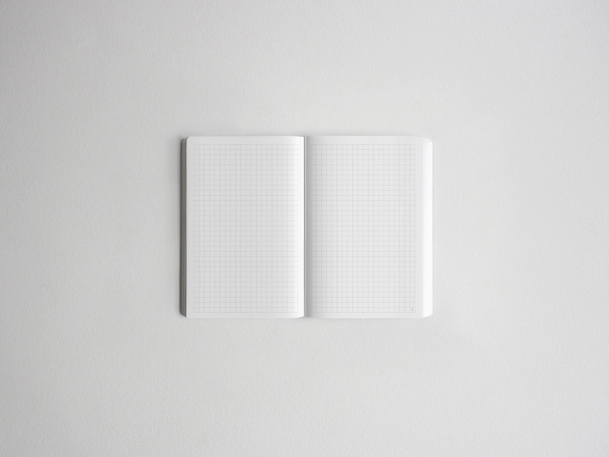 An open white grid notebook or planner with two blank pages, photographed from above on a light gray background.