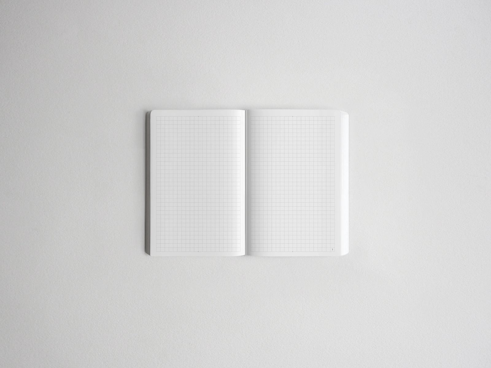 An open white grid notebook or planner with two blank pages, photographed from above on a light gray background.