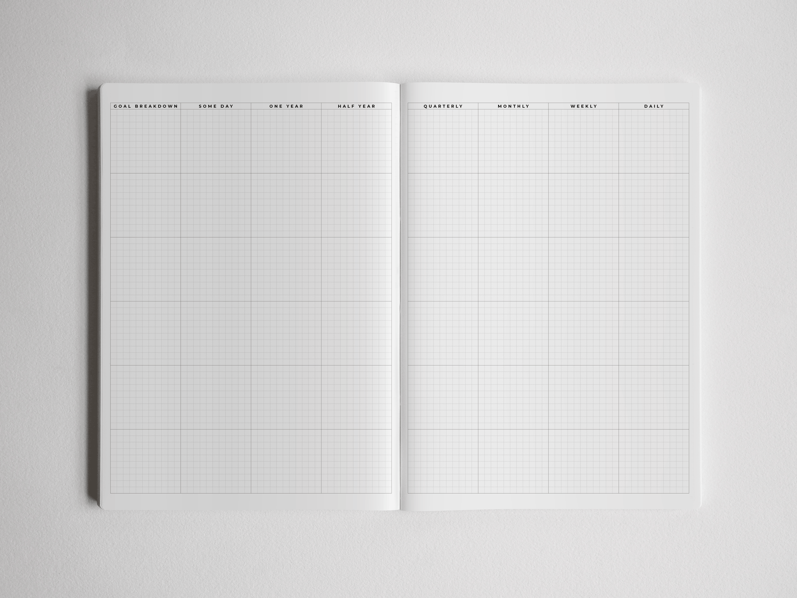 Open academic planner featuring white gridded pages with structured layouts for goal breakdowns, quarterly, monthly, weekly, and daily planning.
