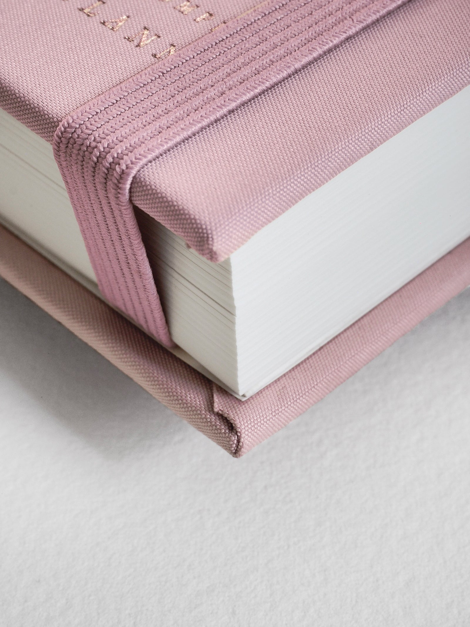 A close-up of a hardcover notebook with a dusty pink fabric cover and matching elastic closure, showing white pages and a textured surface.
#Color_Seashell