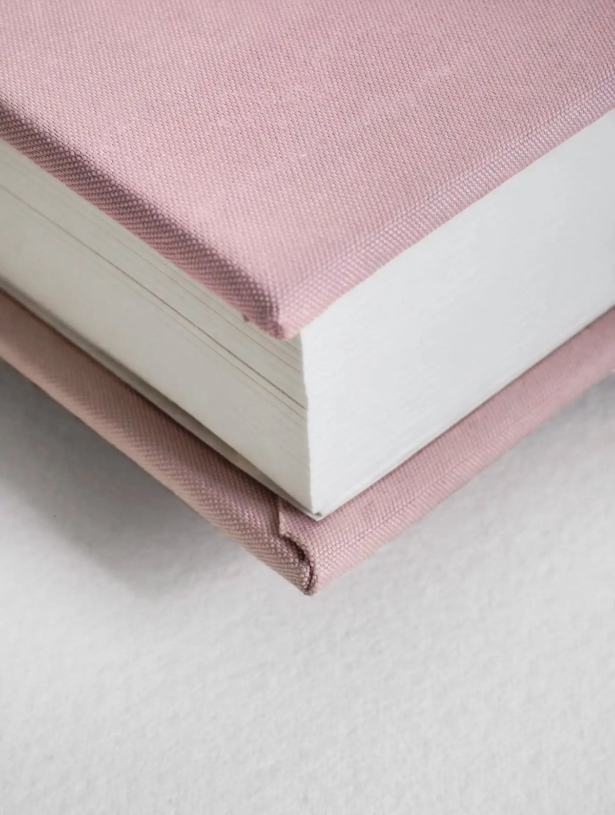 A close-up of a hardcover notebook with a dusty pink fabric cover and matching elastic closure, showing white pages and a textured surface.
#Color_Seashell