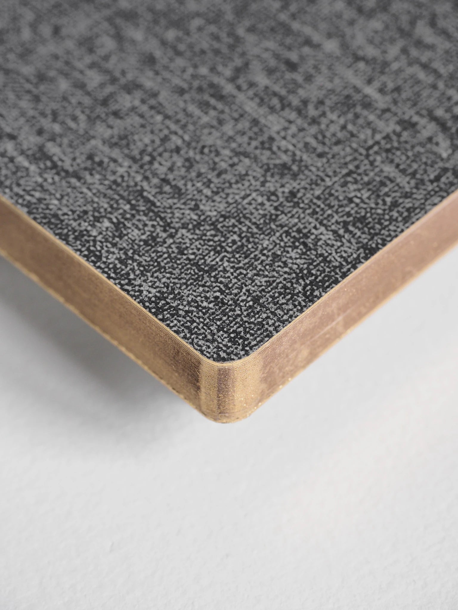 A close-up of a notebook or book corner showing a textured gray cover and white page edges on a light neutral background.
#Color_Tweed