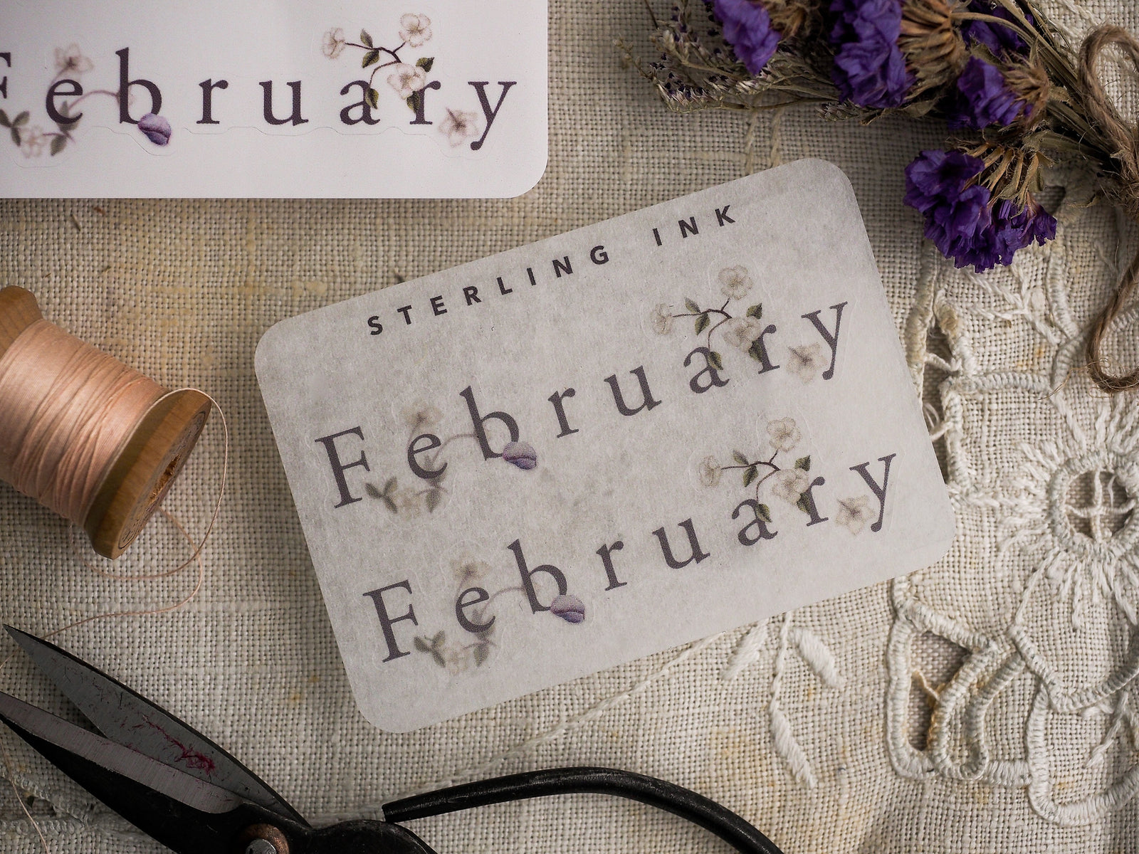 Decorative "February" month stickers featuring delicate, hand-stamped purple floral clusters and elegant "Sterling Ink" lettering, perfect for journaling or planning.
