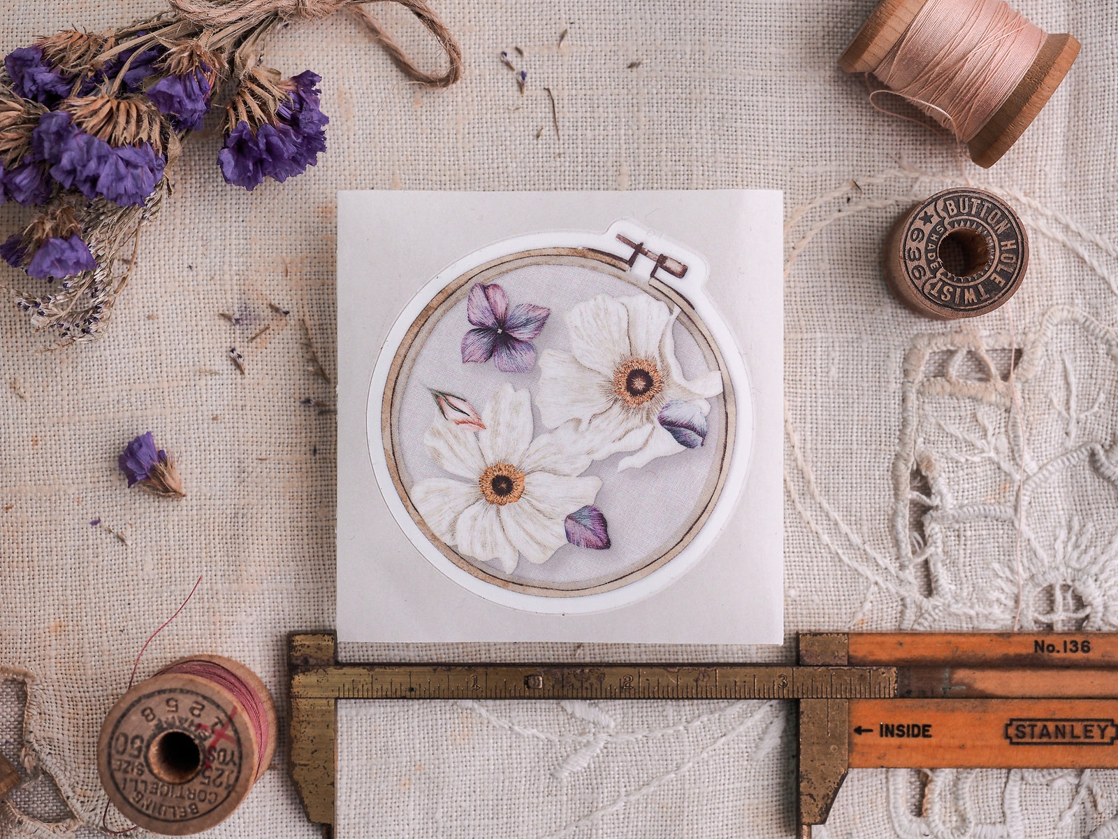 Delicate round die-cut sticker featuring a cluster of white and soft lavender daisies, perfect for floral scrapbook embellishment.