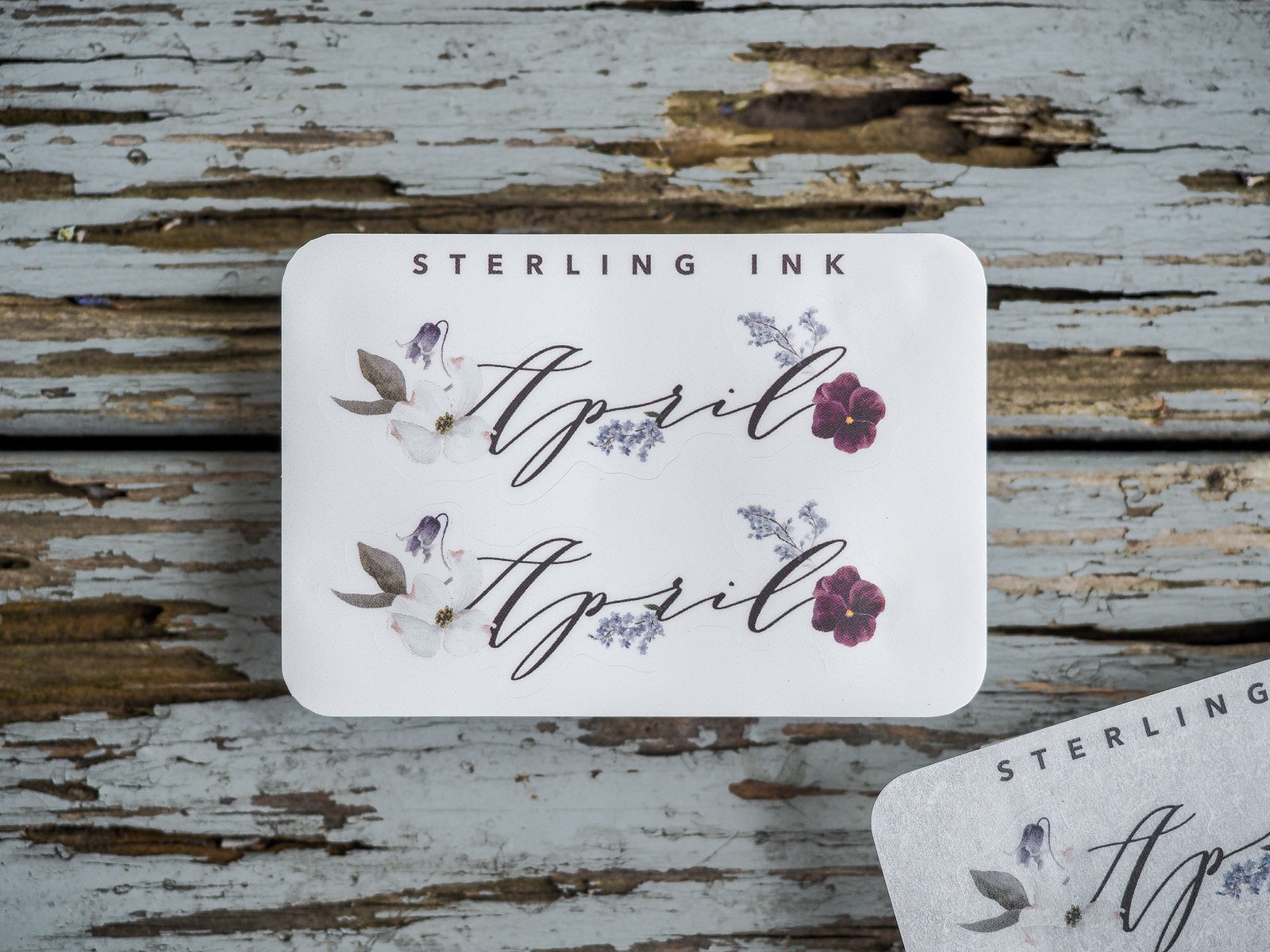 Elegant sticker sheet for April featuring the word "April" in flowing script surrounded by delicate white and purple floral accents.