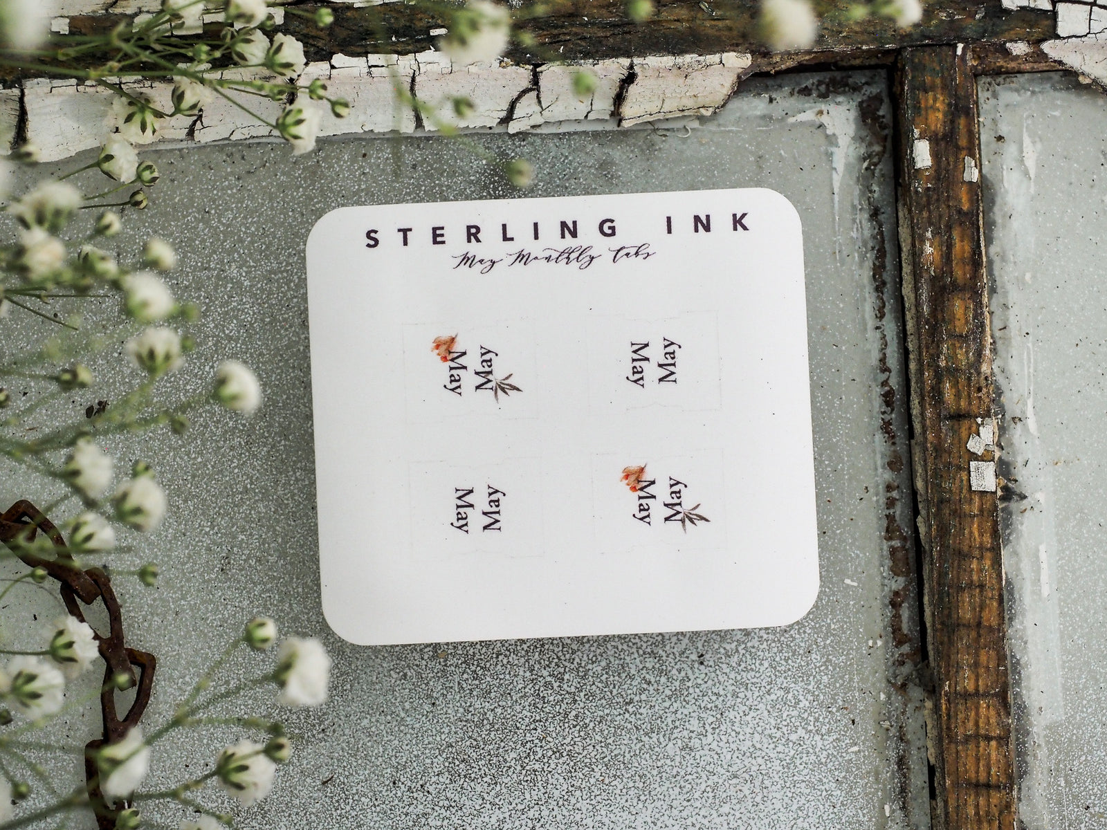 White monthly planning tabs from Sterling Ink, featuring the word "May" printed multiple times beneath small, delicate reddish-brown floral accents.