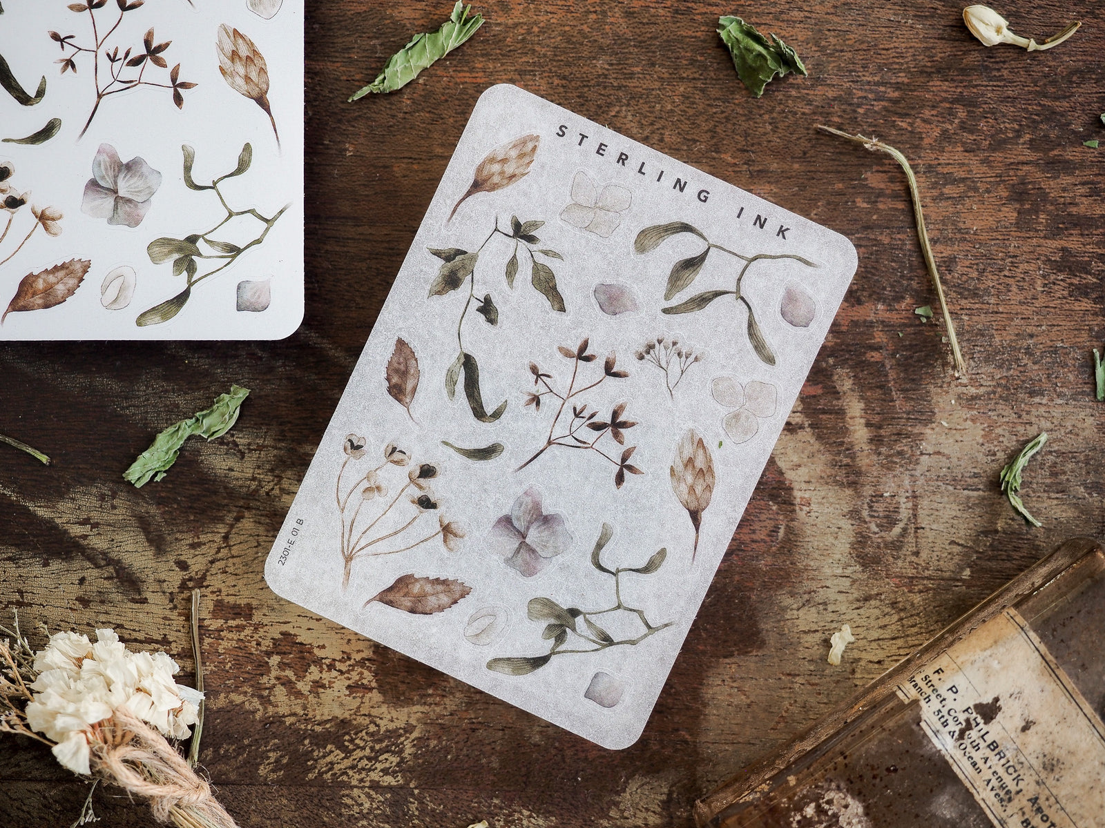 A sticker sheet displaying detailed botanical elements, including delicate leaves, small flowers, and stems, printed in muted earthy tones of green and brown.