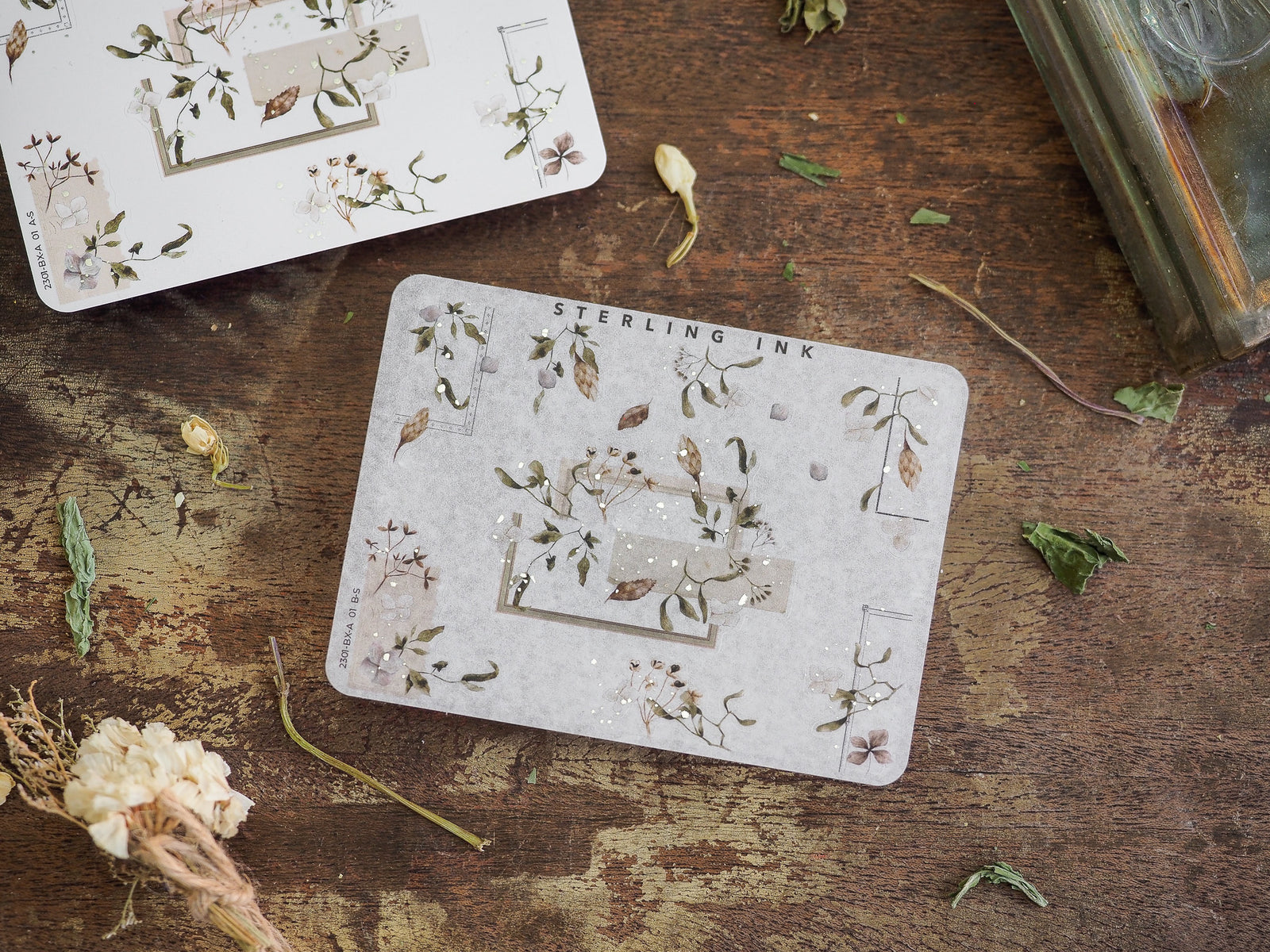 Elegant botanical corner stickers featuring pressed leaves and wildflowers arranged around silver foil-accented border designs.