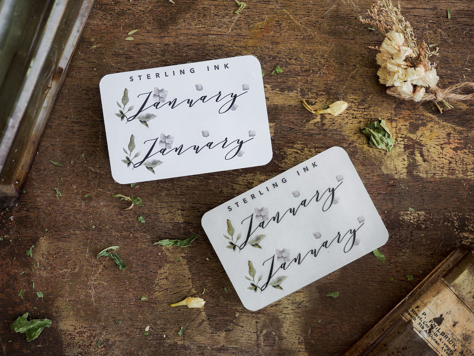 Elegant white month stickers featuring "January" in script, delicately adorned with scattered watercolor leaves and small natural floral accents.
