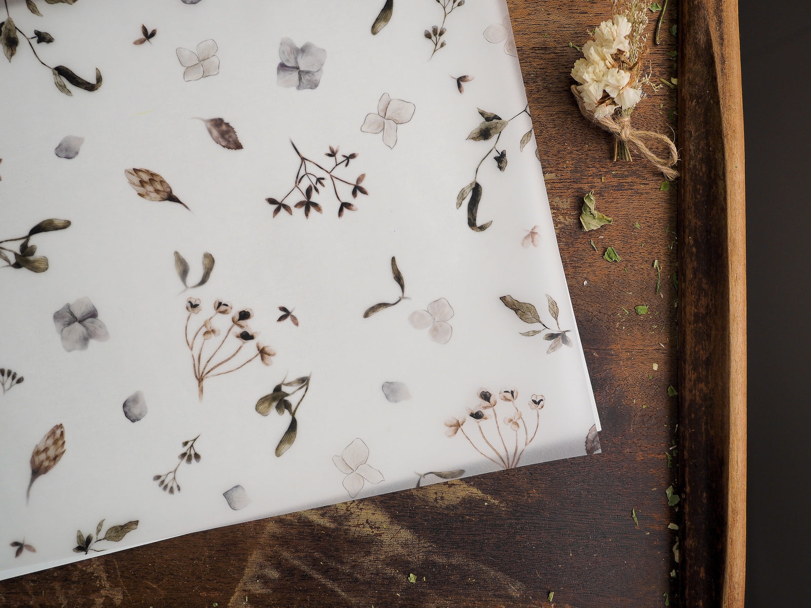Delicate vellum sheet featuring a subtle, scattered pattern of watercolor botanical illustrations, including delicate leaves and small spring blossoms.