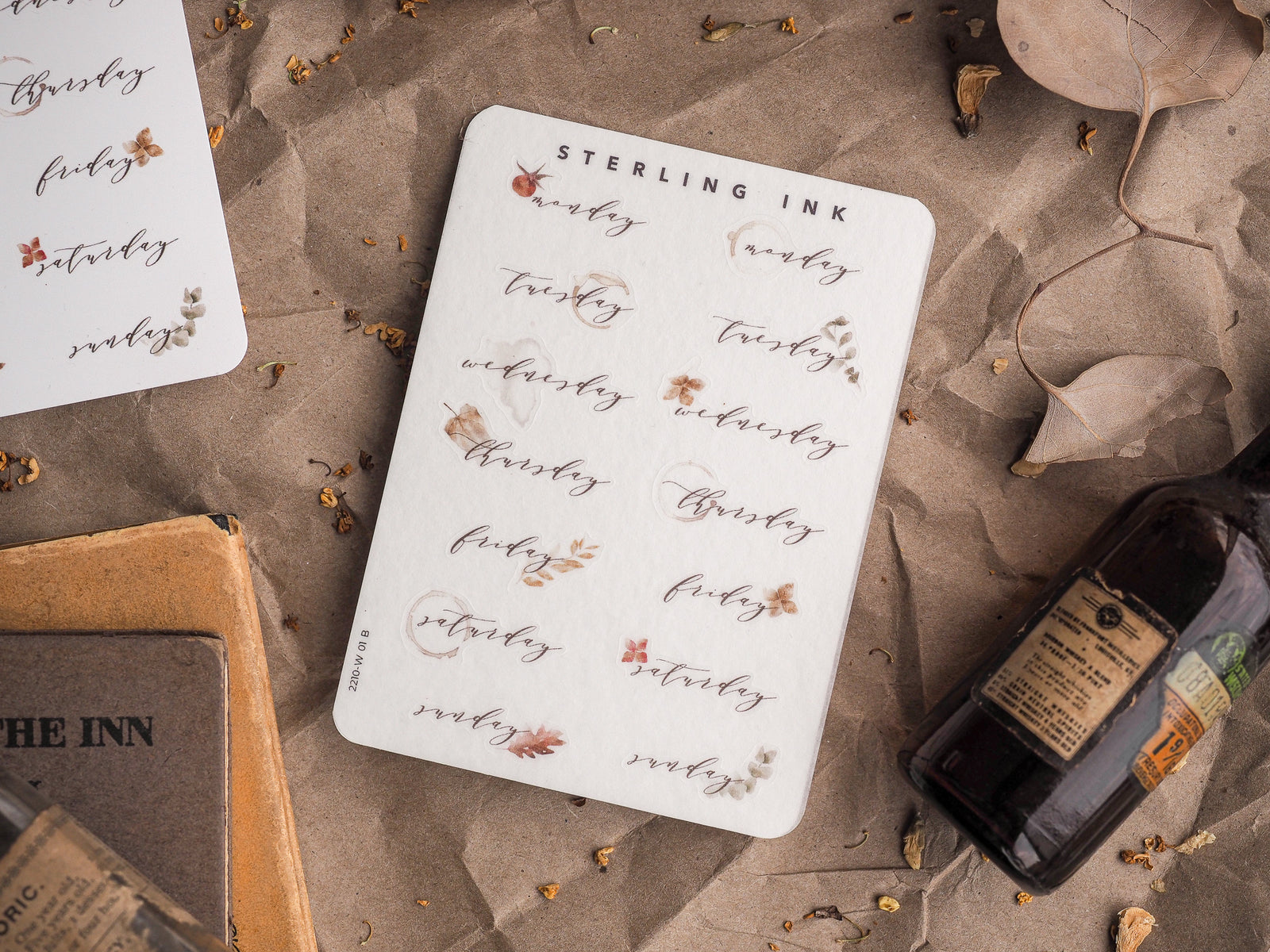Decorative sticker sheet with rustic, hand-lettered days of the week, each accented by delicate gold leaves and botanical elements.