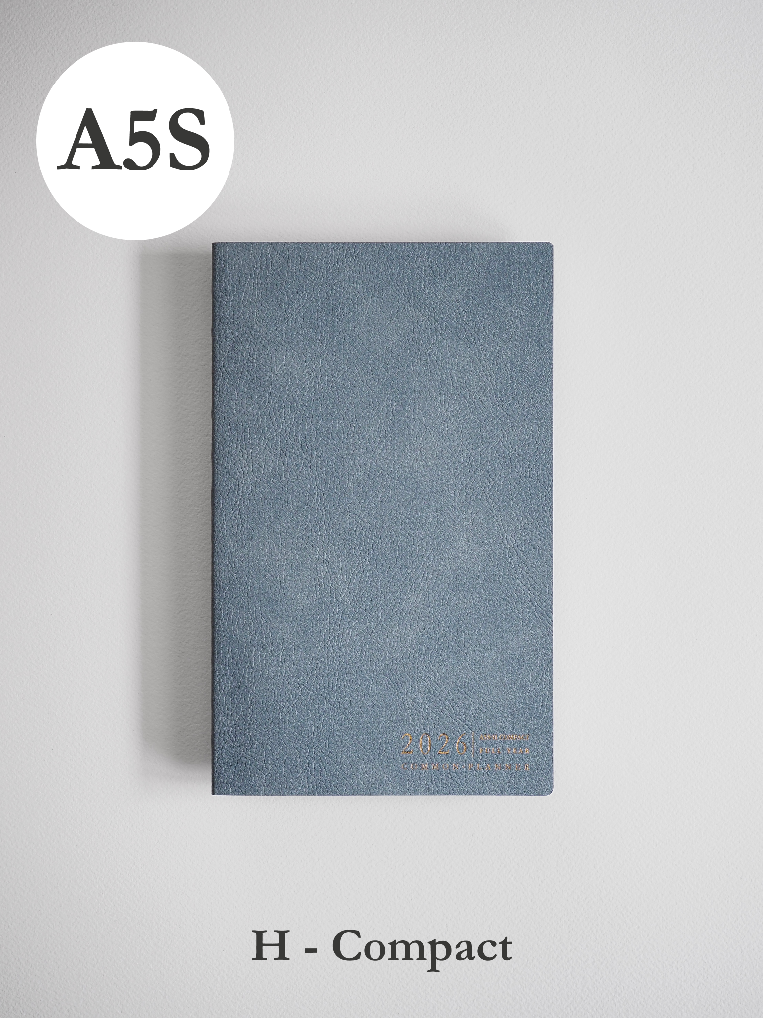 Compact A5 planner bound in slate blue faux leather, subtly embossed with the year 2026 in metallic gold lettering.