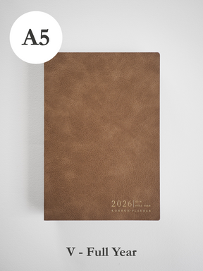 A minimalist A5 planner cover in a rich, earthy tan tone, featuring centered embossed text that reads "2026 Full Year Common Planner."