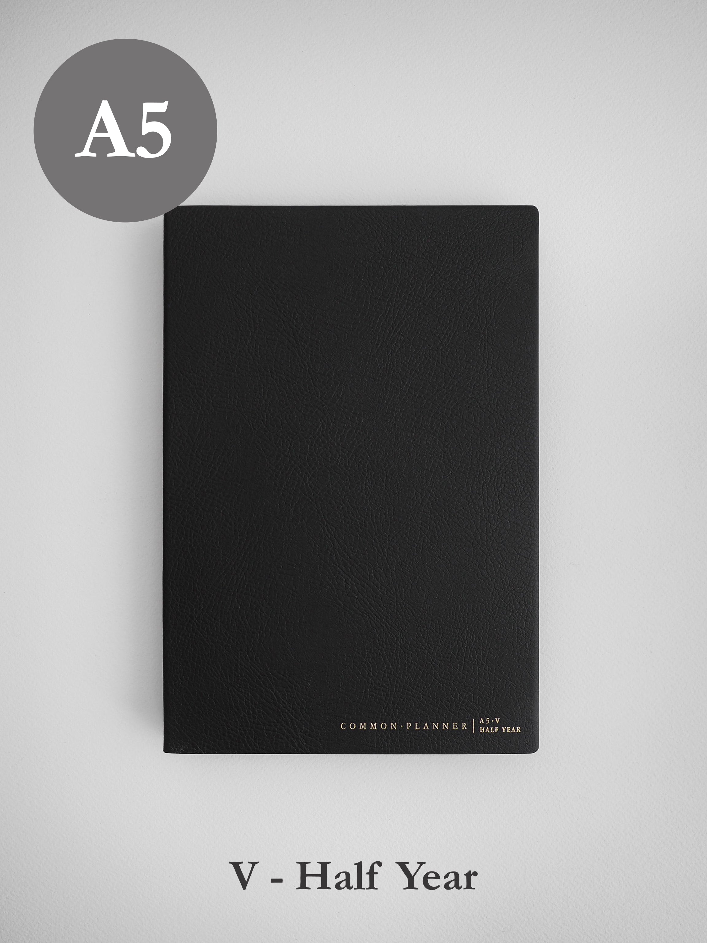 A sleek, matte black A5 common planner for half year use, designed with a minimalist aesthetic and featuring subtle branding along the bottom edge.