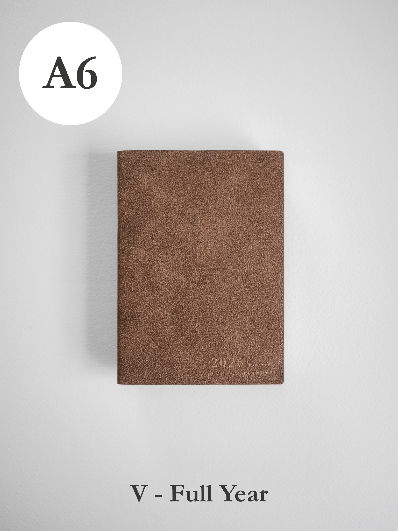 Minimalist A6 vertical planner in a warm taupe faux leather, featuring the embossed text "2026" for organization.