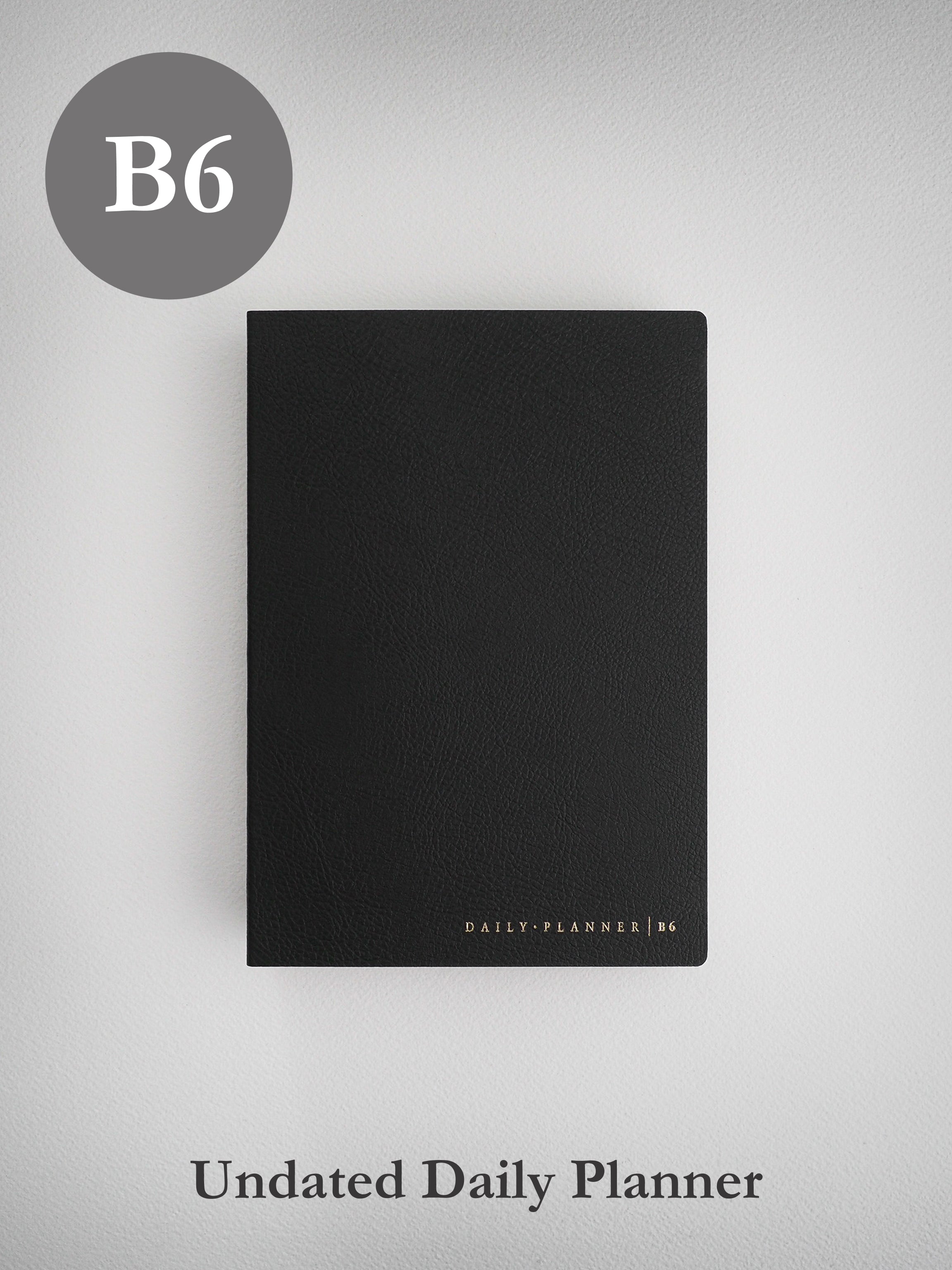 A matte black B6 daily planner journal featuring a structured, textured cover and subtle gold-toned branding near the bottom.