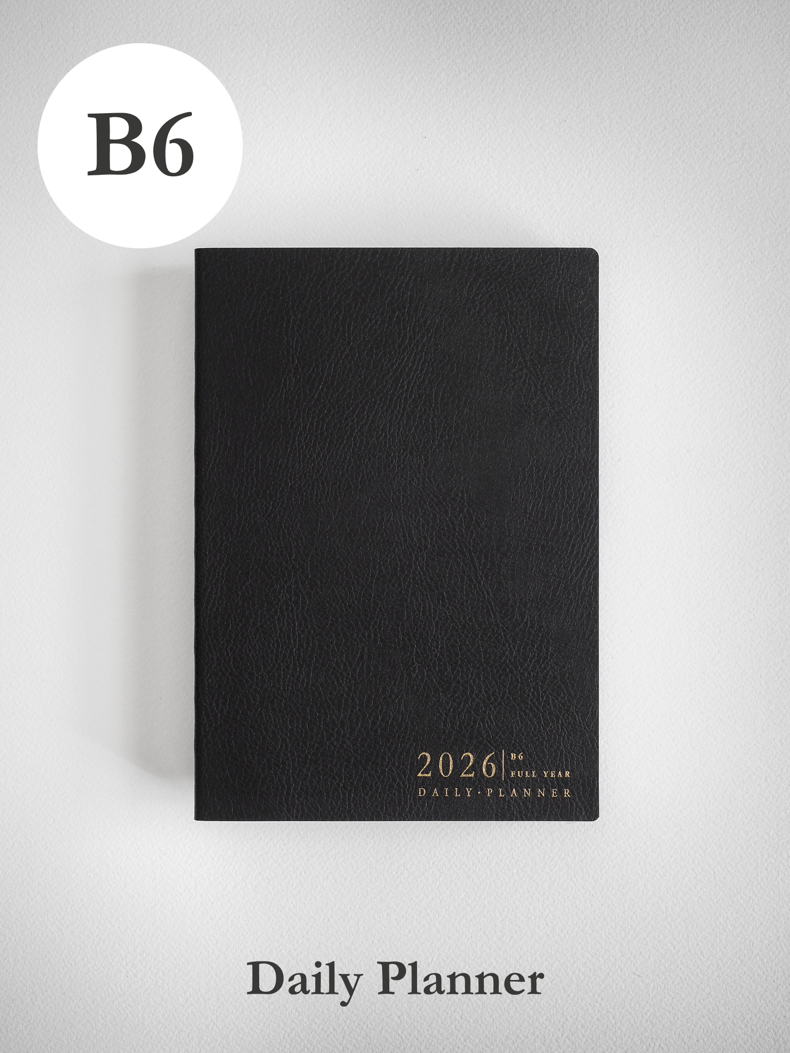 Sleek black B6 daily planner with a matte, textured cover, featuring white embossed text that reads 2026 Full Year Daily Planner.