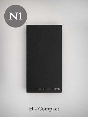 Sleek, black, undated planner journal with a textured cover, labeled "Common Planner N1 Compact Full Year," designed for organized scheduling.