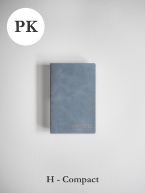 Compact, horizontally oriented planner in dusty slate blue, featuring a matte finish and the year 2026 visible on the front cover.