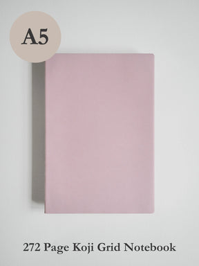 A pink A5 size koji grid notebook shown against a light gray background, with a beige circle label reading 'A5' in the top left and text at the bottom reading '272 Page Koji Grid Notebook'.
#Color_Fairyfloss