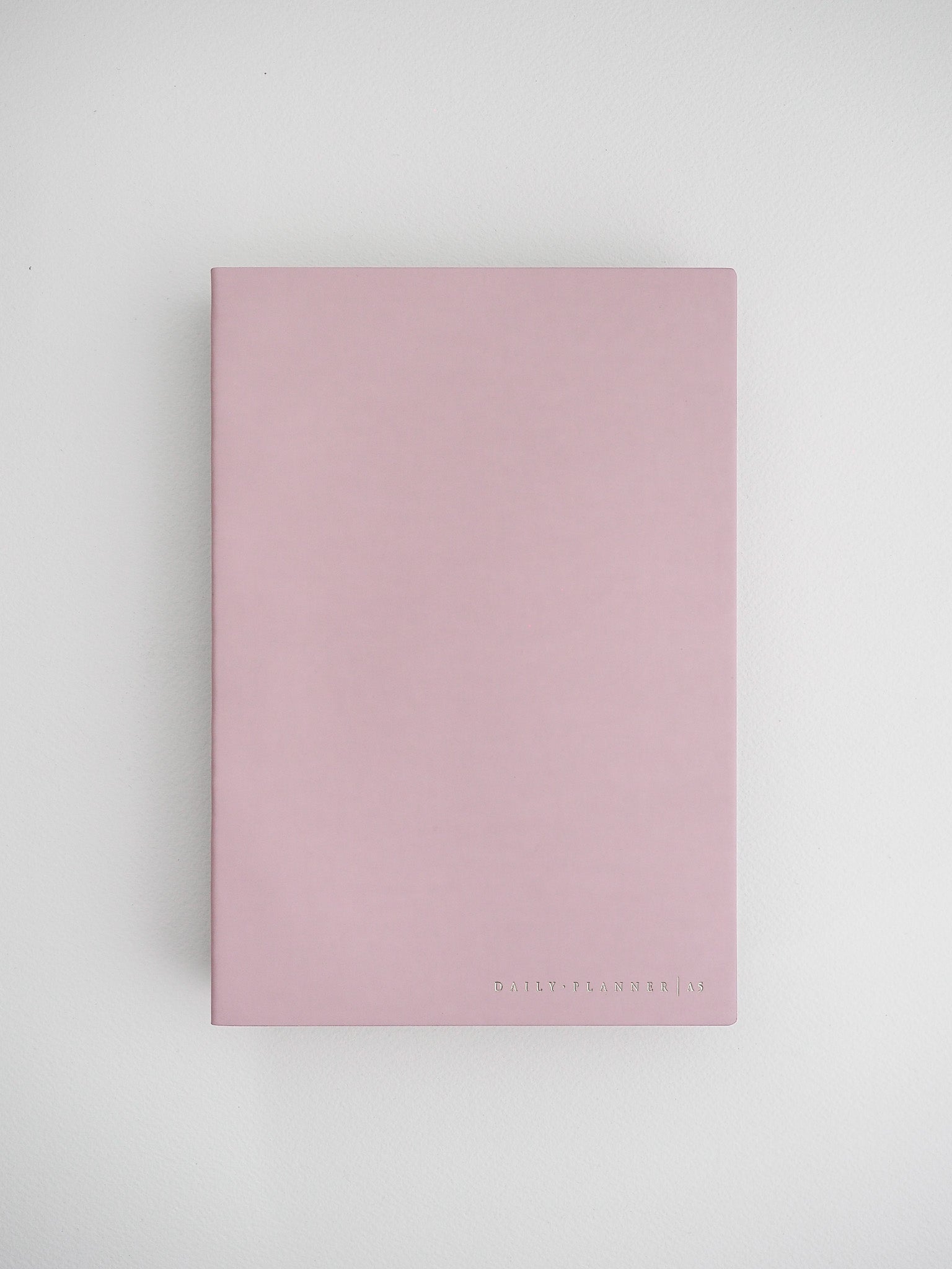 A minimalist, solid blush pink planner cover with the brand name "DAILY PLANNER" debossed near the bottom center.