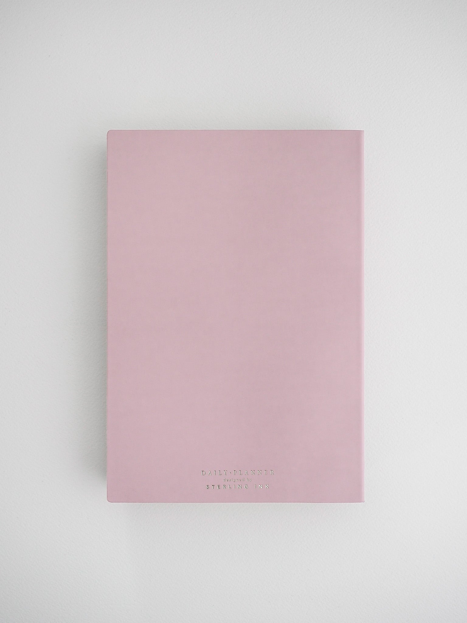 Elegant blush pink daily planner notebook with a clean, solid cover and minimal black branding, perfect for journaling or organization.