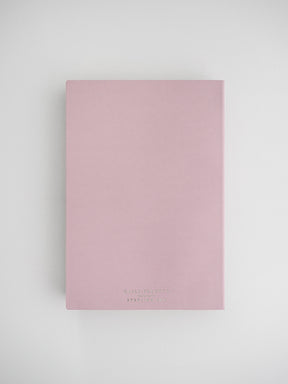 Elegant blush pink daily planner notebook with a clean, solid cover and minimal black branding, perfect for journaling or organization.
