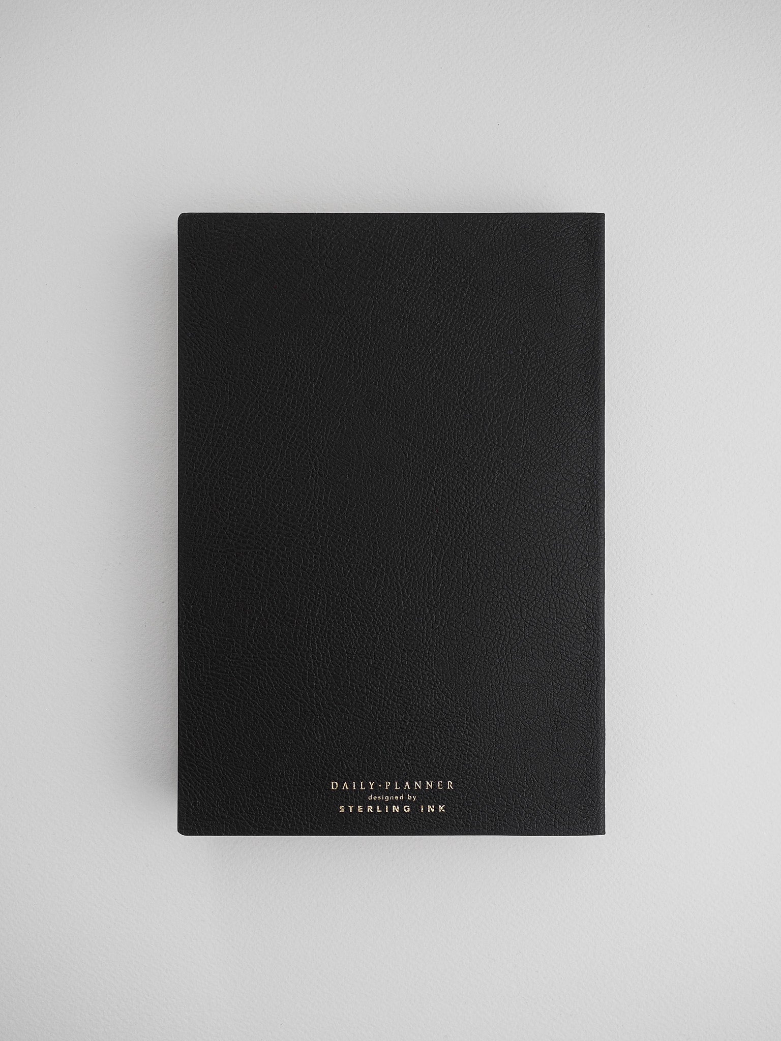 Sleek, black daily planner notebook featuring a textured, leather-like cover and elegant foiled lettering from Sterling Ink.