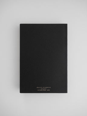 Sleek, black daily planner notebook featuring a textured, leather-like cover and elegant foiled lettering from Sterling Ink.