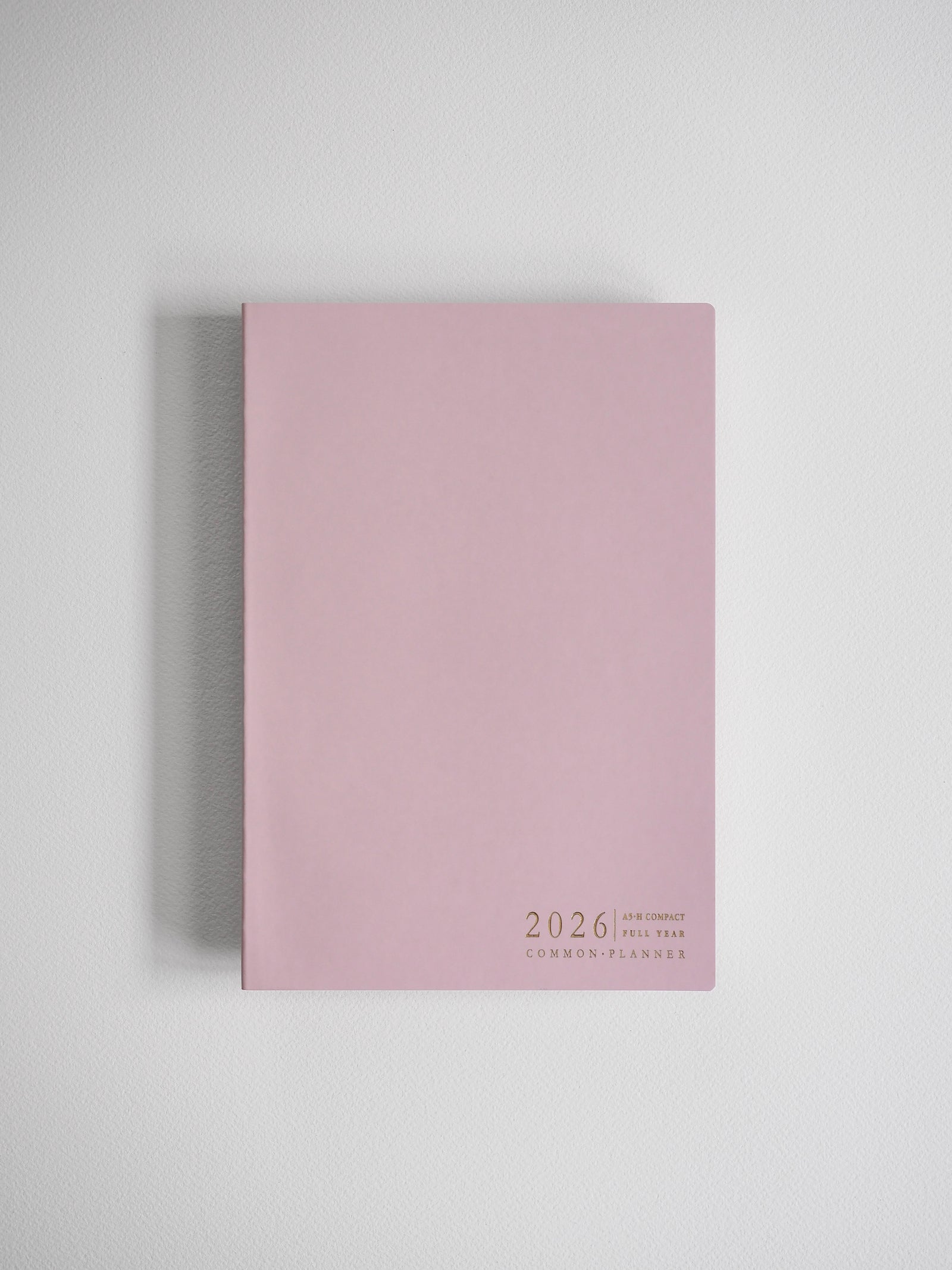 Minimalist A5 planner in solid blush pink featuring centered black text detailing "2026," "Full Year," and the "Common Planner" brand.