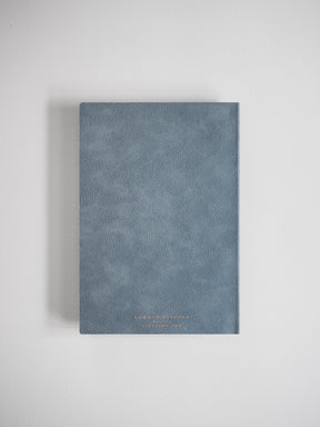 A full-year A5 planner bound in dusty blue faux leather, featuring a sophisticated, minimalist design with subtle gold foil lettering.