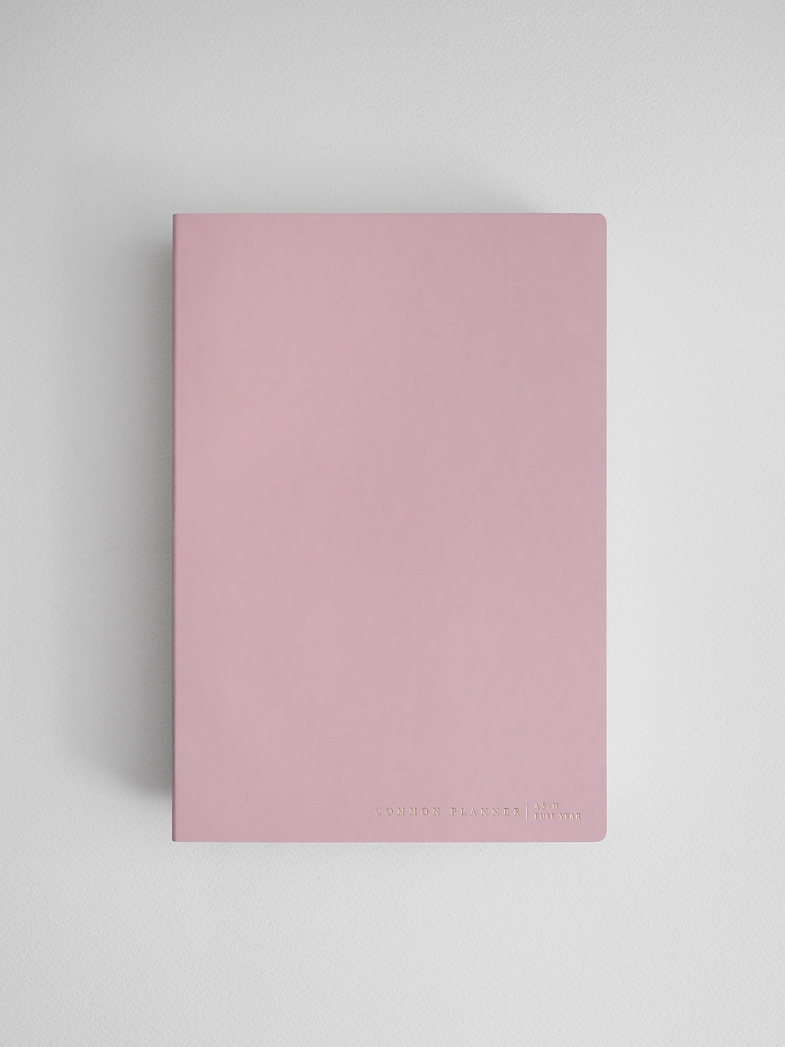Minimalist pale pink common planner for full-year journaling and organization, featuring a clean, solid cover and simple typography.