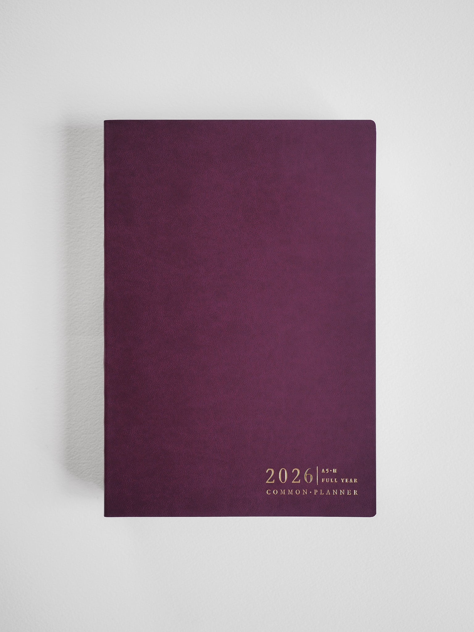 Elegant A5 horizontal planner bound in deep maroon faux leather, featuring minimal, centered gold-toned text for "2026 Common Planner."