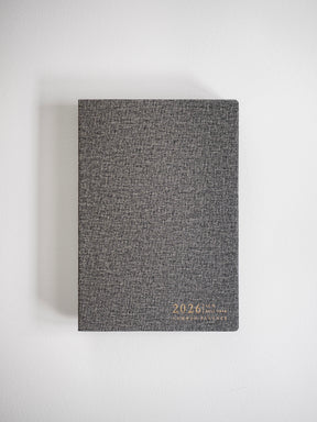 Textured dark gray A5 planner featuring elegant metallic gold foil lettering that displays "2026 Common Planner," ready for a full year of organization.