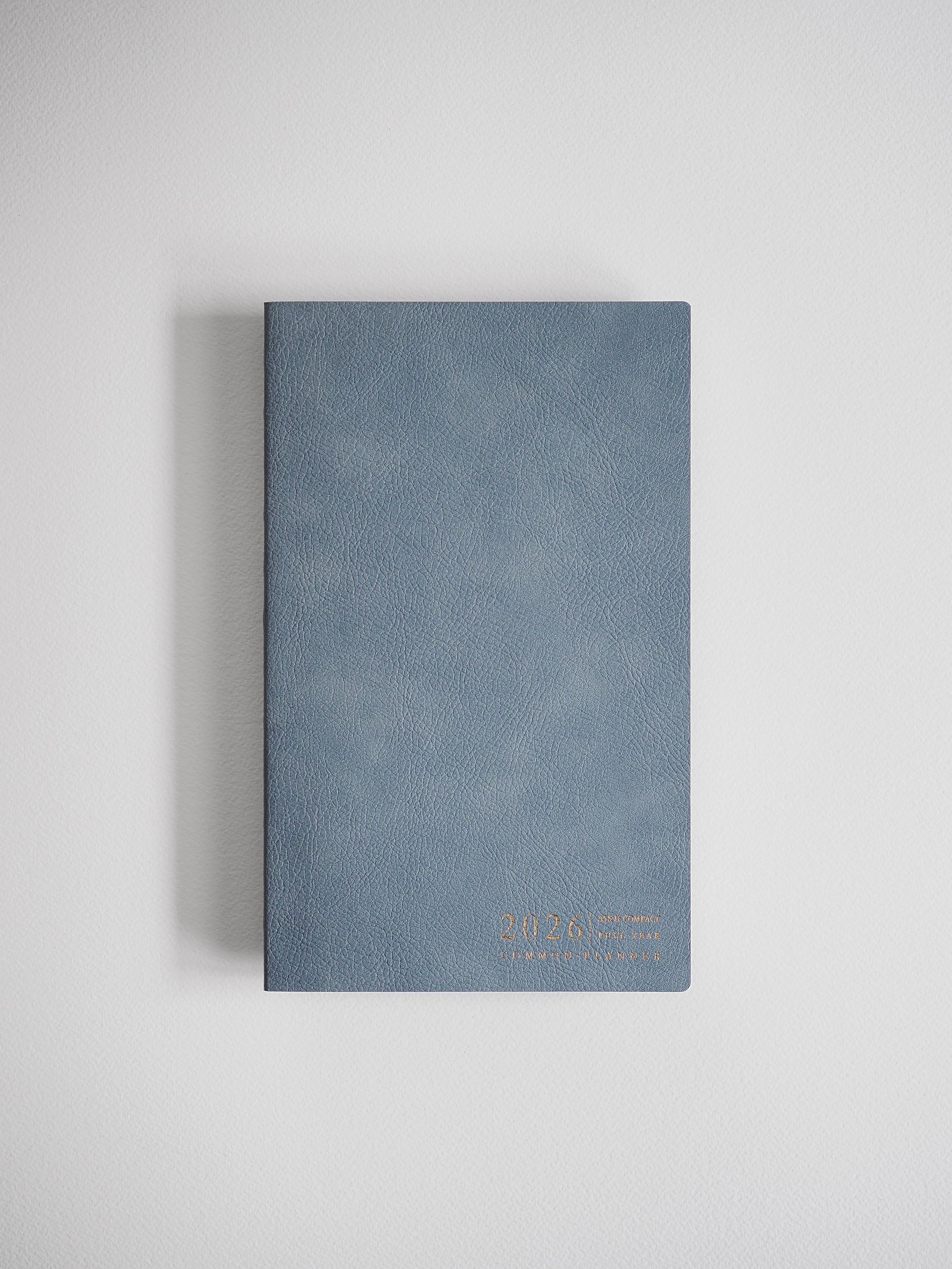 Compact slate blue A5 planner featuring a horizontal layout and accented with elegant gold foil lettering for the 2026 Common Planner.
