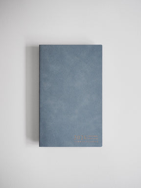 Compact slate blue A5 planner featuring a horizontal layout and accented with elegant gold foil lettering for the 2026 Common Planner.