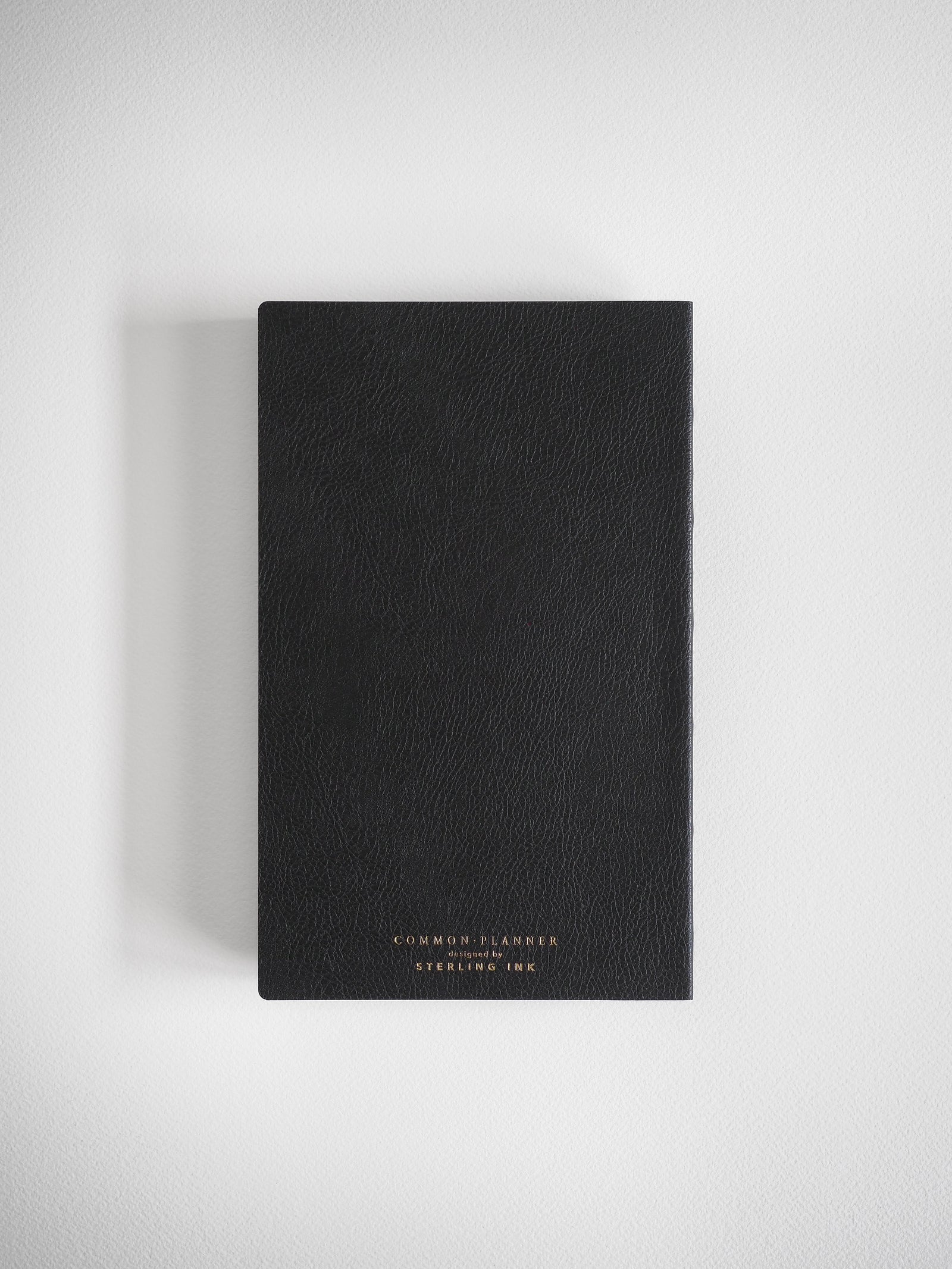 Sleek black A5 planner with a minimalist matte cover, debossed with the professional text "COMMON PLANNER designed by STERLING INK."
