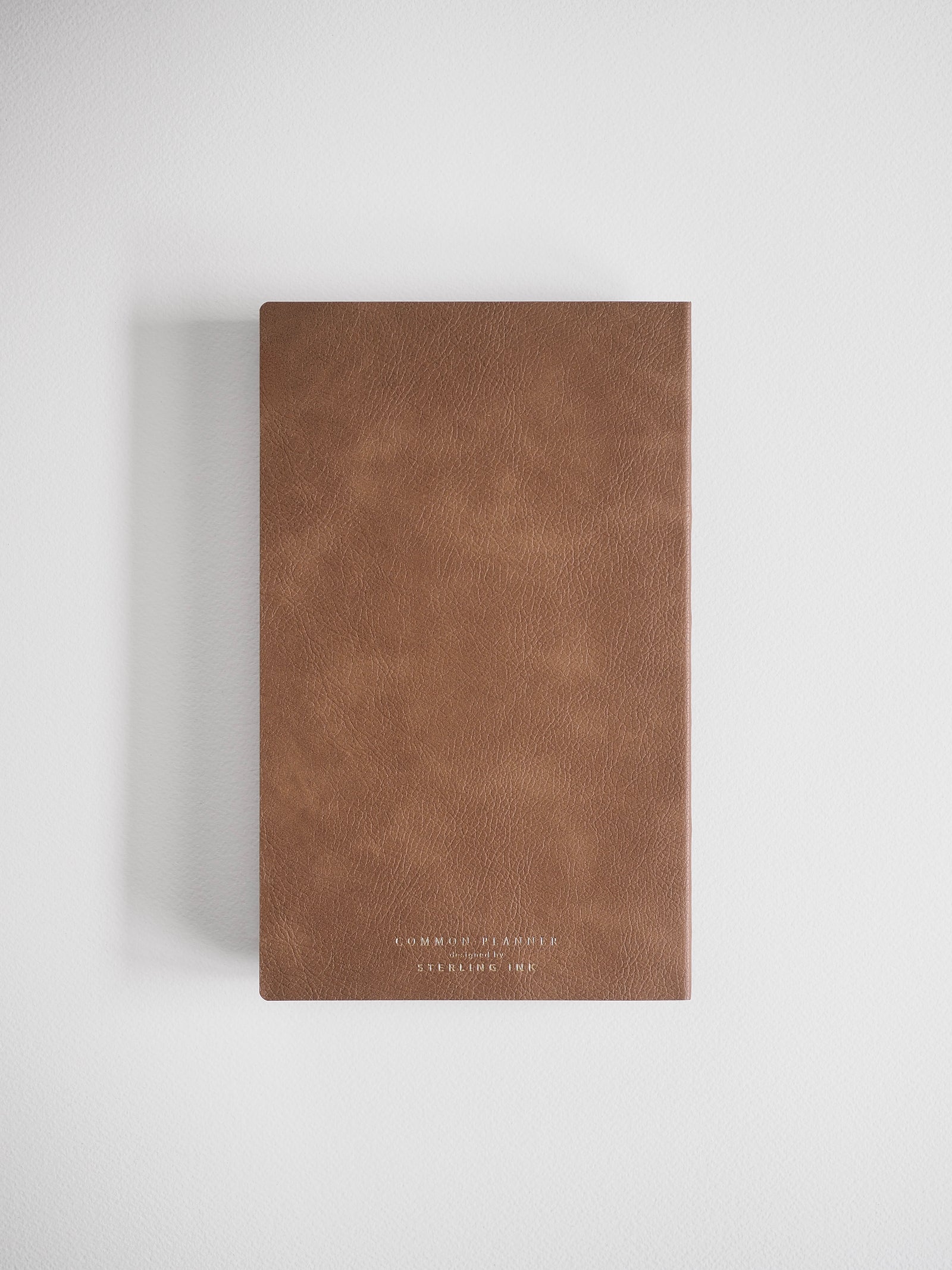 A slim, deep cocoa-brown planner featuring a minimalist design and embossed branding for 'COMMON PLANNER' and 'STEELING INK'.