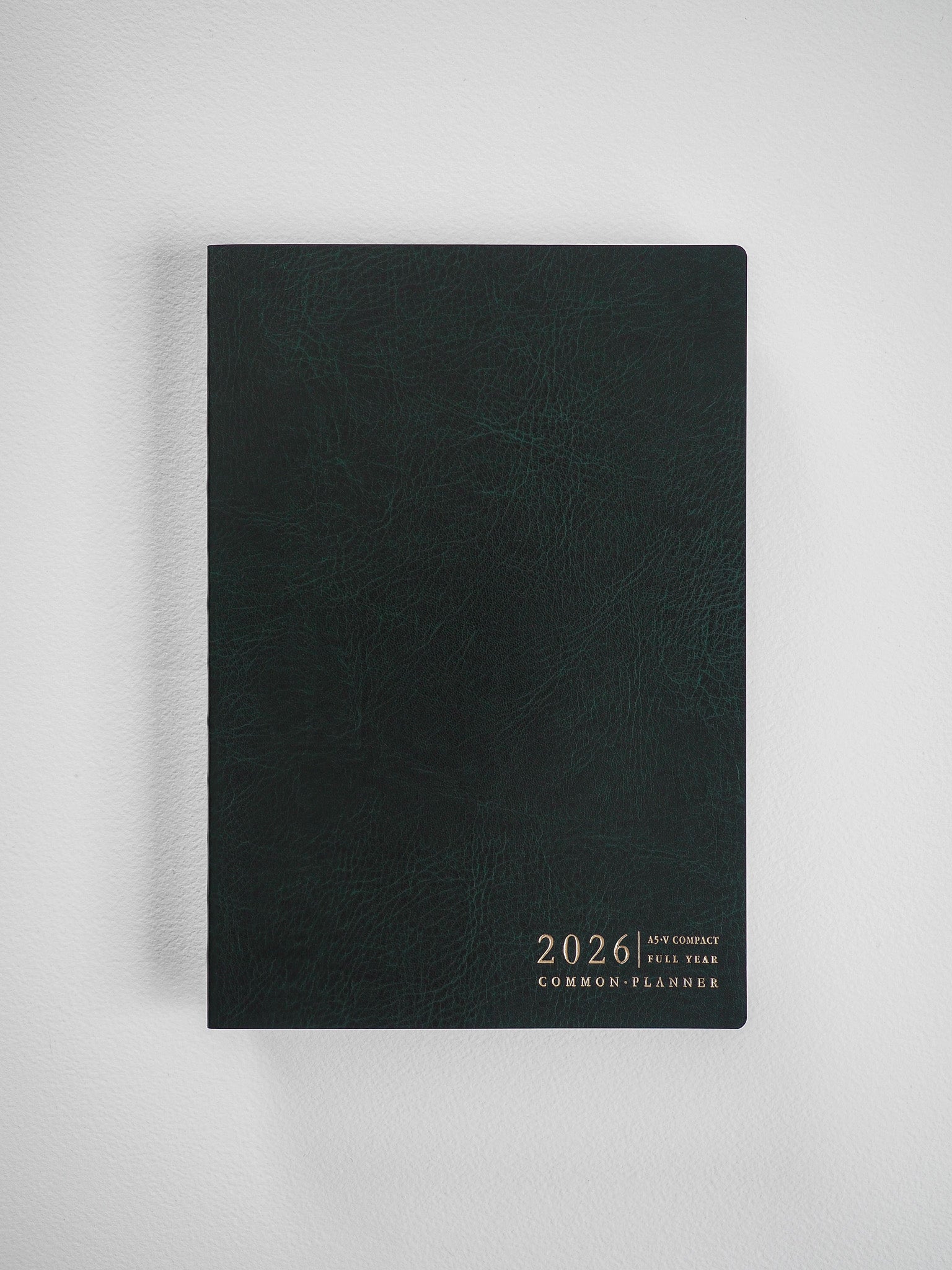 Deep charcoal A5 compact planner cover featuring centrally embossed gold lettering for "2026 A5 V. Compact Full Year Common Planner."
